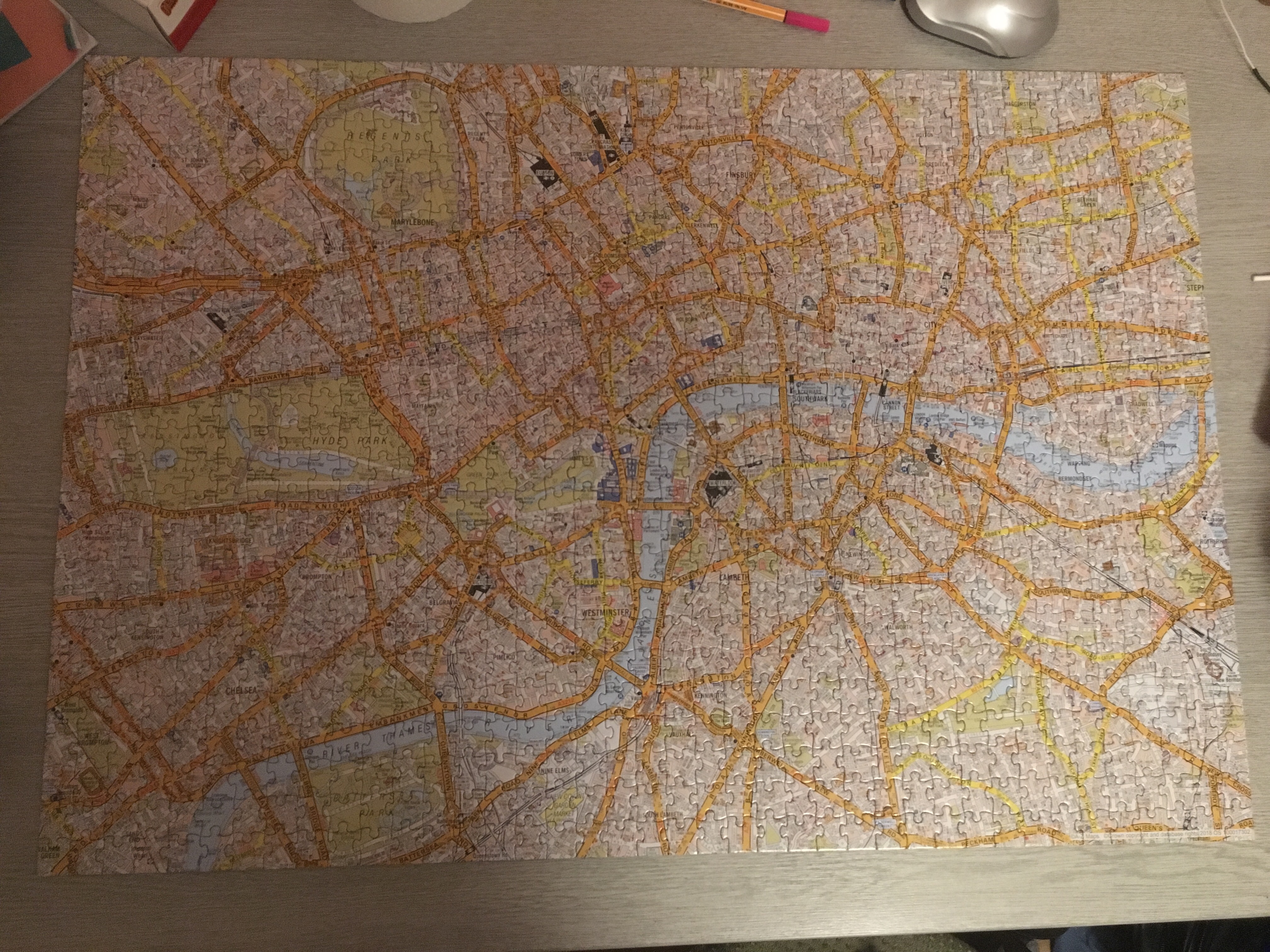 A jigsaw of an A–Z map of central London. The map sits on a grey wood-effect desk, with various bit of desk clutter around it (including a pen).