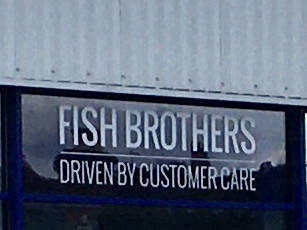 A darkened window beneath corrugated metal walling. Text in the window, in white capital letters, says “Fish Brothers, driven by customer care”.