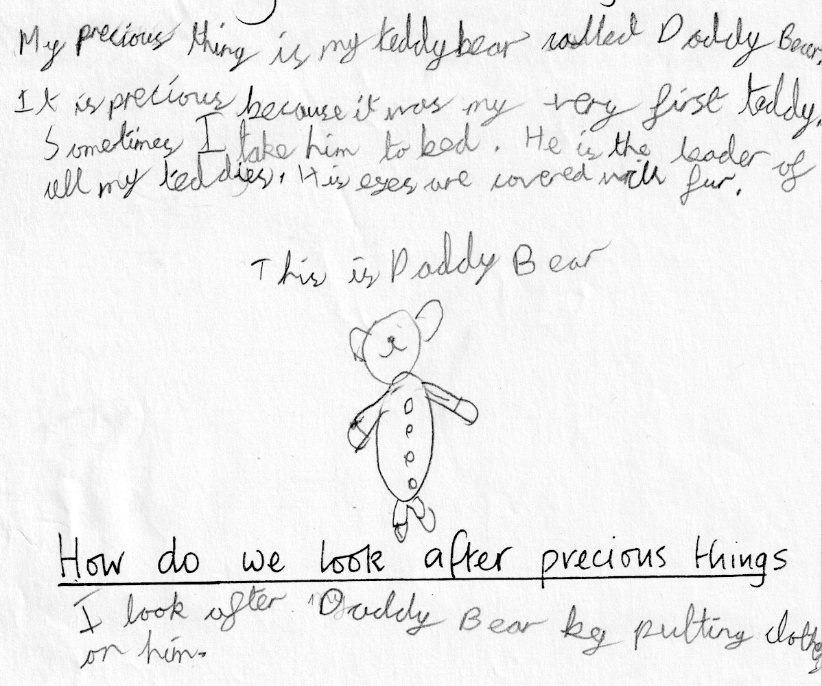 A section of a worksheet, filled in by a child. In child's handwriting, it says: "My precious thing is my teddy bear called Daddy Bear. It is precious because it was my ver first teddy. Sometimes I take him to bed. He is the leader of all my teddies. His eyes are covered with fur. This is Daddy Bear." There is then a child's line drawing of a teddy bear with buttons down his front. Underneath, in the teacher's handwriting (as a prompt on the worksheet), it says "How do we look after precious things", and underneath the child's response says "I look after Daddy Bear by putting clothes on him."